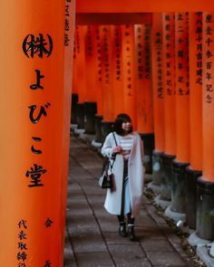 a woman walking down a sidewalk under tall orange pillars with writing on it's sides