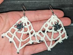 a hand holding two small crocheted spider earrings