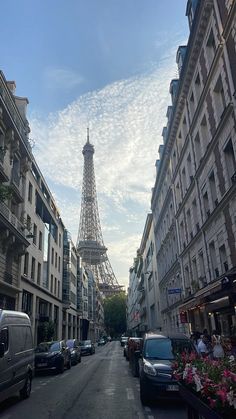 the eiffel tower is in the distance as cars are parked on the street