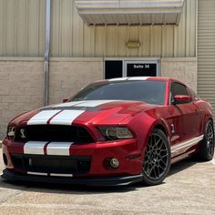 a red and white mustang parked in front of a building