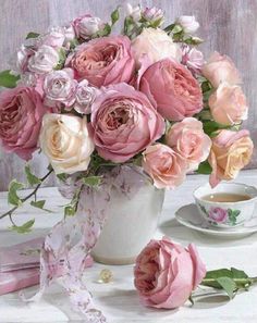 a vase filled with lots of pink flowers next to a cup and saucer