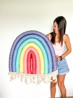 a woman standing next to a giant rainbow shaped pillow with tassels on it