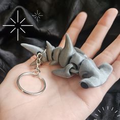 a hand holding a keychain with a toy shark on it's back