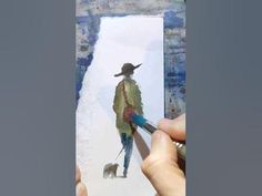 a person is holding a paintbrush and drawing with watercolors on white paper