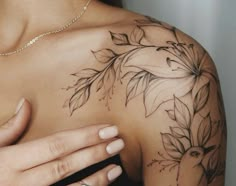 a close up of a woman's shoulder with flowers and leaves tattooed on it