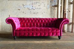 a red velvet couch sitting in front of a white brick wall with exposed piping