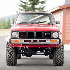 a red jeep is parked in front of a building with trees on the other side