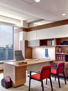 an office with two red chairs and a desk in front of a large window overlooking the city