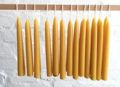 yellow candles are hanging on a clothes line against a white brick wall with wooden pegs