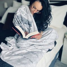 a woman reading a book while sitting on a bed covered in sheets and blankets with her eyes closed