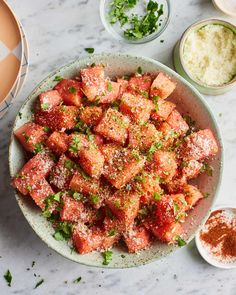 a white plate topped with meat covered in seasoning next to bowls of other food