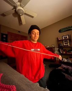 a man in a red shirt is holding a rope with his hands while standing next to a couch