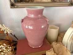 a pink vase sitting on top of a wooden table next to a painting and candles