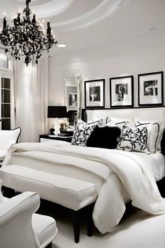 a white bedroom with black and white accessories on the bed, chandelier and chair