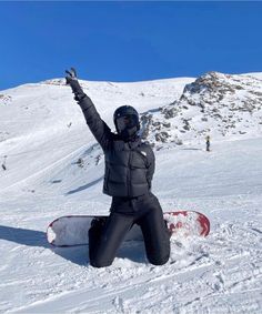 a snowboarder sitting on the ground with his arms in the air and one hand up