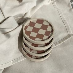 four wooden coasters sitting on top of a white cloth covered tablecloth with brown and white checkerboard design