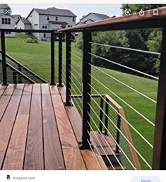 a wooden deck with black railing and handrails in front of houses on a green lawn