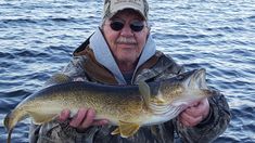 a man holding a large fish in his hands on the side of a body of water