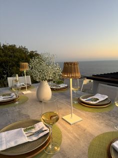 an outdoor dining area overlooking the ocean at sunset with wine glasses, plates and utensils