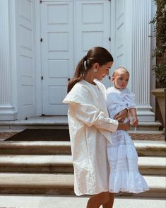 a woman holding a baby in her arms while walking up some steps with another person