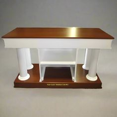 a white and brown table with columns on it's sides, in front of a gray background