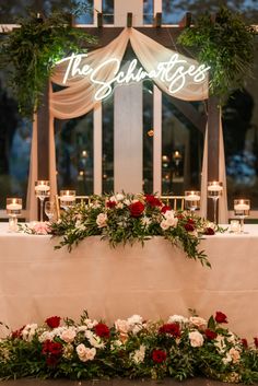 the table is set with flowers and candles for an elegant wedding reception in front of a lit up sign