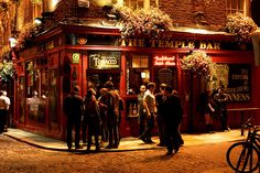 a group of people standing outside of a bar at night time in front of a brick building