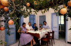 three people sitting at a table with food and drinks in front of an orange tree