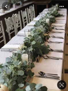 a long table is set up with place settings and greenery for the centerpieces