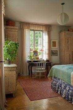 a bedroom with a bed, desk and chair next to a large wooden cabinet in front of a window