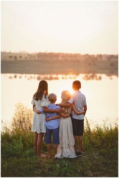 a group of people standing next to each other near a body of water at sunset