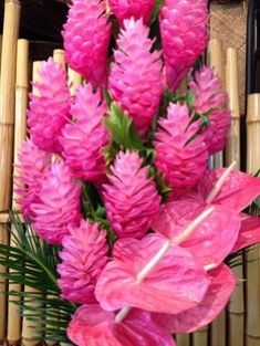 pink flowers are in a vase next to bamboo sticks and a window with shutters