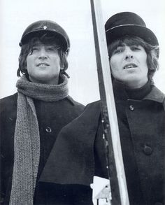 two people wearing hats and scarfs standing next to each other with ski poles in front of them