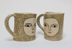 two coffee mugs with faces on them sitting next to each other in front of a white background