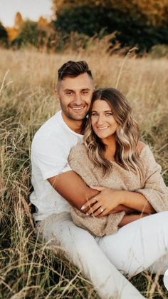 a man and woman are sitting in the tall grass with their arms around each other