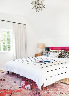 a bed room with a neatly made bed next to a window and a rug on the floor