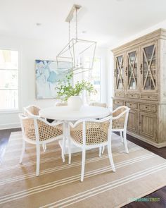 a dining room table with wicker chairs and a white vase on top of it