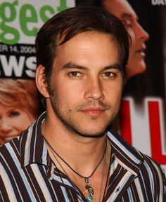 a man in striped shirt standing next to a wall with movie posters on the background