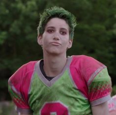 a young man with green hair wearing a pink and green football jersey is staring at the camera