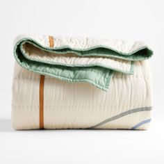 a white and green blanket laying on top of a bed next to an orange striped pillow