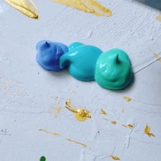 three small blue and green animals sitting on top of a white surface next to paintbrushes