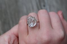 a close up of a person's hand holding a ring with an oval shaped diamond