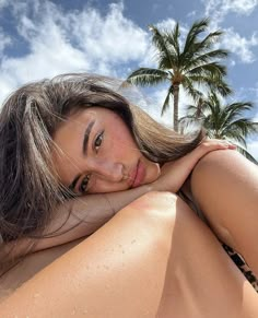 a beautiful woman laying on top of a sandy beach next to palm trees and blue sky