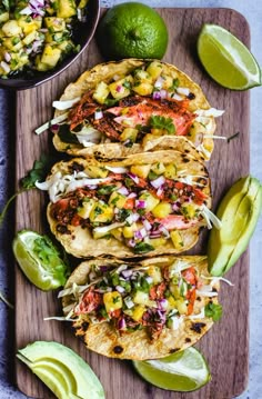 three tacos on a cutting board with avocado and salsa