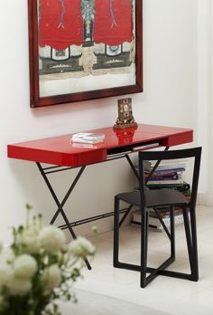 a red table sitting next to a painting on the wall