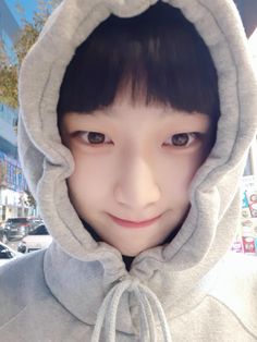 a young person wearing a hoodie and looking at the camera while standing in front of a building