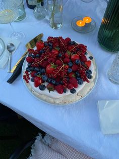 a cake with berries and blueberries on it sitting on a table next to candles