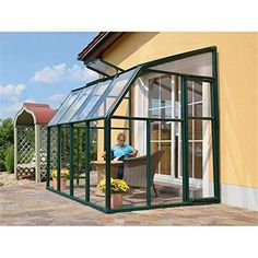 a woman sitting at a table in front of a green house with a glass roof