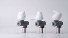 three white birds sitting on top of small cylinders in front of a white background,