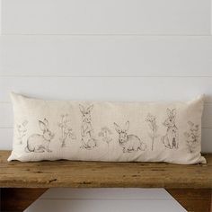 a white pillow with black drawings of rabbits on it sitting on a wooden bench next to a wall